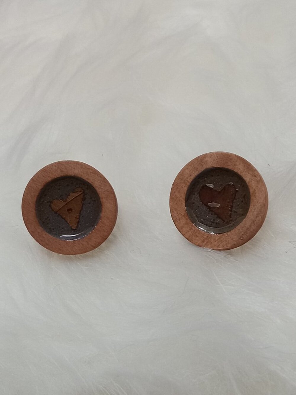 Handmade earrings on a wooden base with a piece of punched-out tree leaf